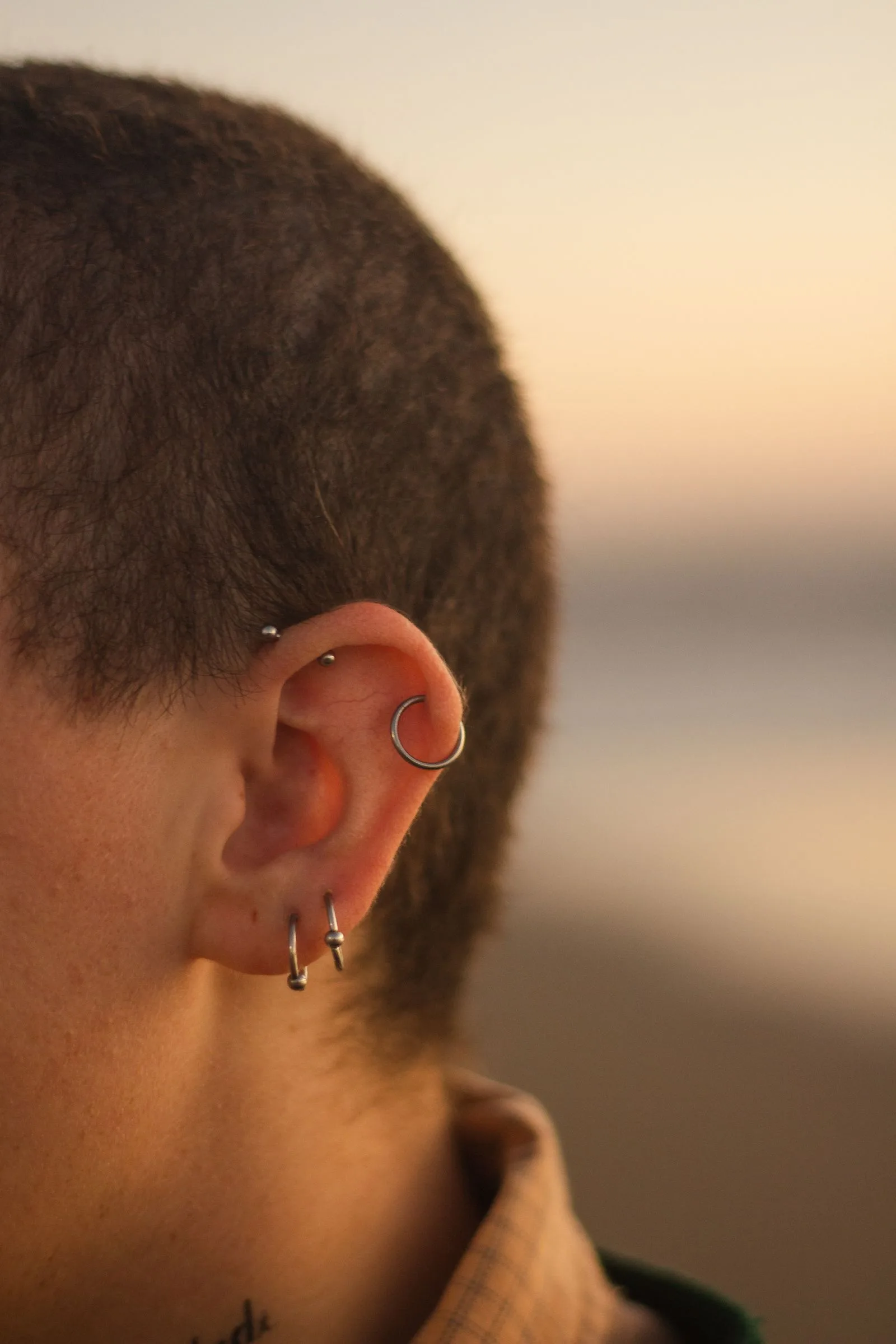 Gros plan d'une oreille portant plusieurs piercings achetés à l'unité sur le lobe et l'hélix