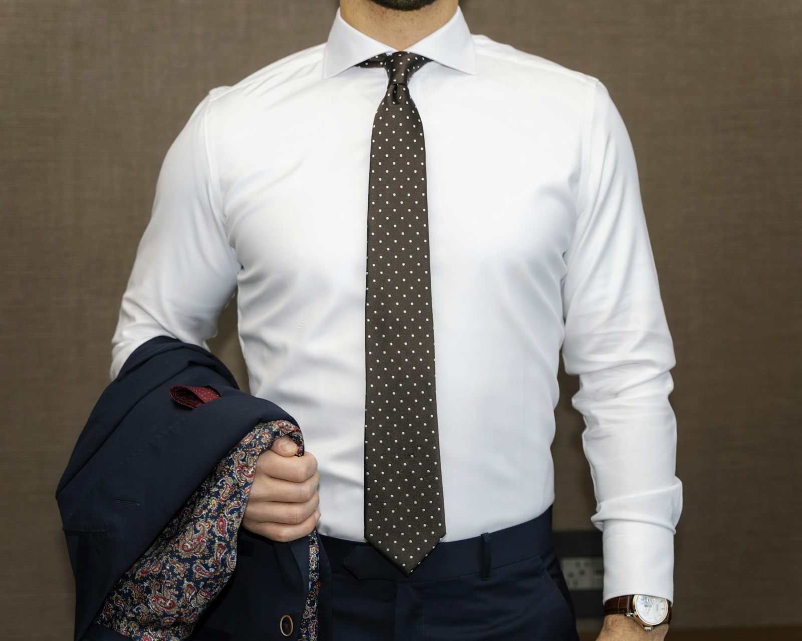 Homme en chemise blanche habillée avec cravate à pois et veste de costume marine sur le bras