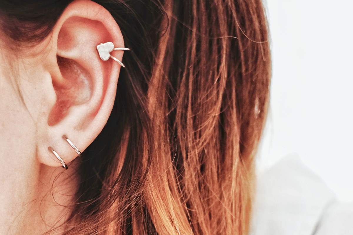 Oreille portant trois piercings : deux anneaux au lobe et un bijou en forme de cœur à l'hélix